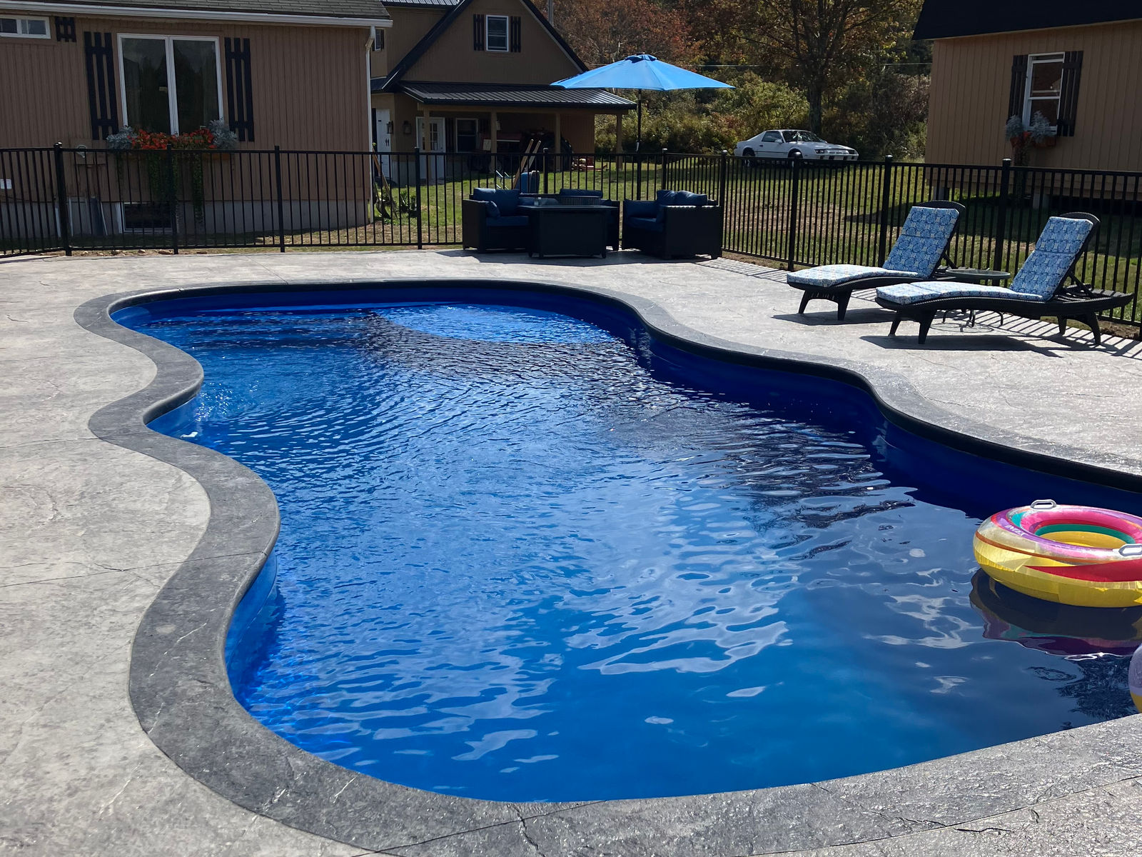 Brilliant blue freeform fiberglass pool with a shaded pavilion and open countryside views
